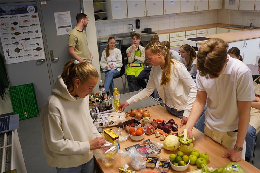 Tre ungdommer undersøker matrester som er spredd utover en kjøkkenbenk - Klikk for stort bilde