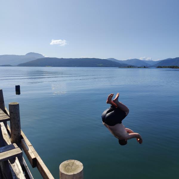 Mann i badebukse midt i en salto ut i vannet