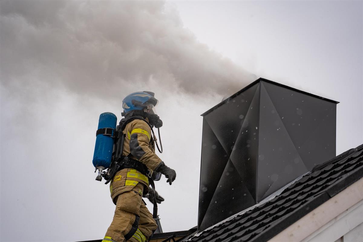 brannkonstabel på tak vedsiden av pipehatt med mye røyk - Klikk for stort bilde