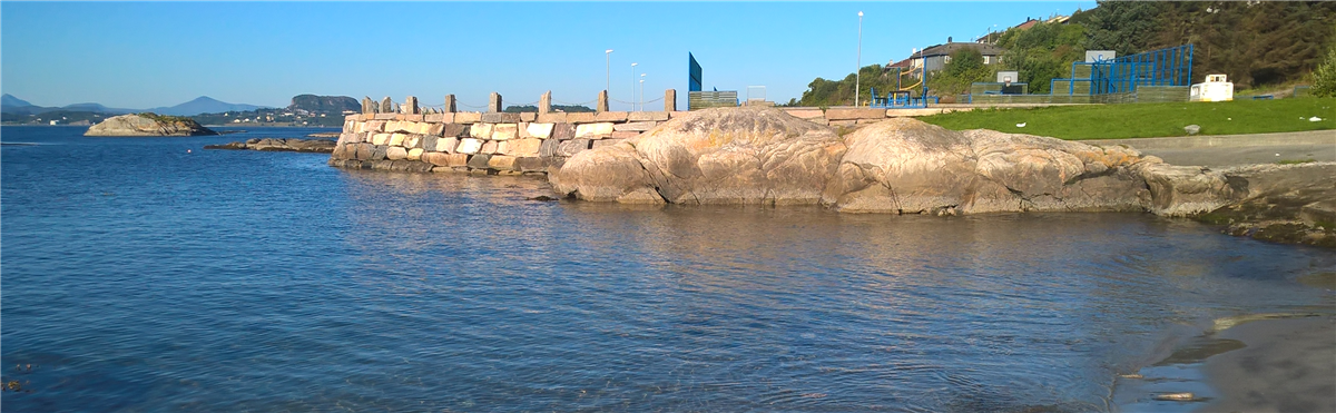 Bilde som viser strandlinjen ved Skjærva med volleyballbanene i bakgrunnen - Klikk for stort bilde