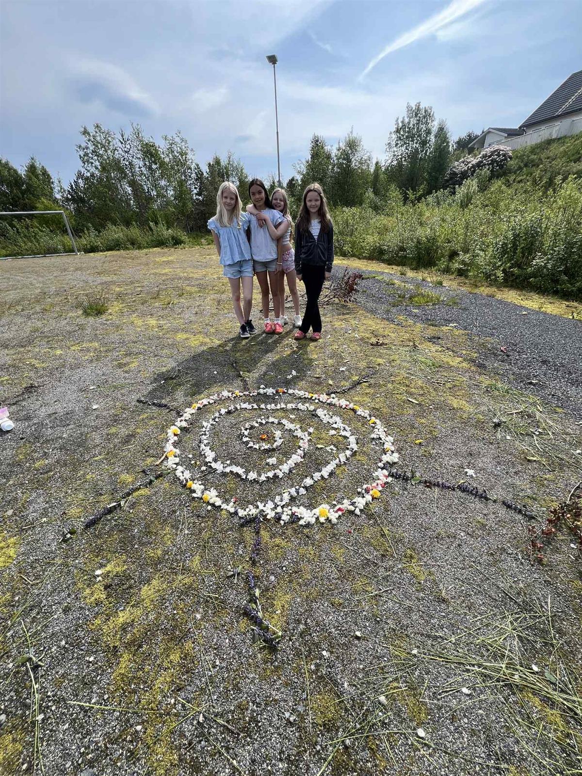 På bildet ser vi fire elever som viser fram sin "sol" som de har lagd av ulike planter og blomster de har funnet liggende på bakken i området.  - Klikk for stort bilde