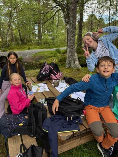 Bildet viser fire elever som smiler og viser fram plantefunnene sine i bakgrunn. - Klikk for stort bilde