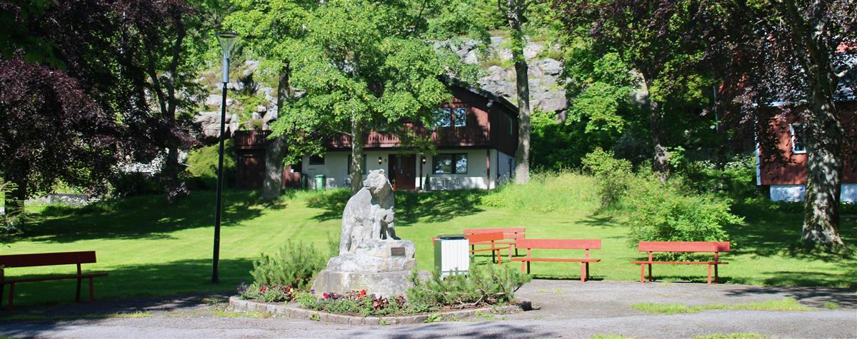 Bilde som viser utsikt over parken med statuen av bjørnen sentral og benker rundt et gresskledd område skjermet med trær. - Klikk for stort bilde